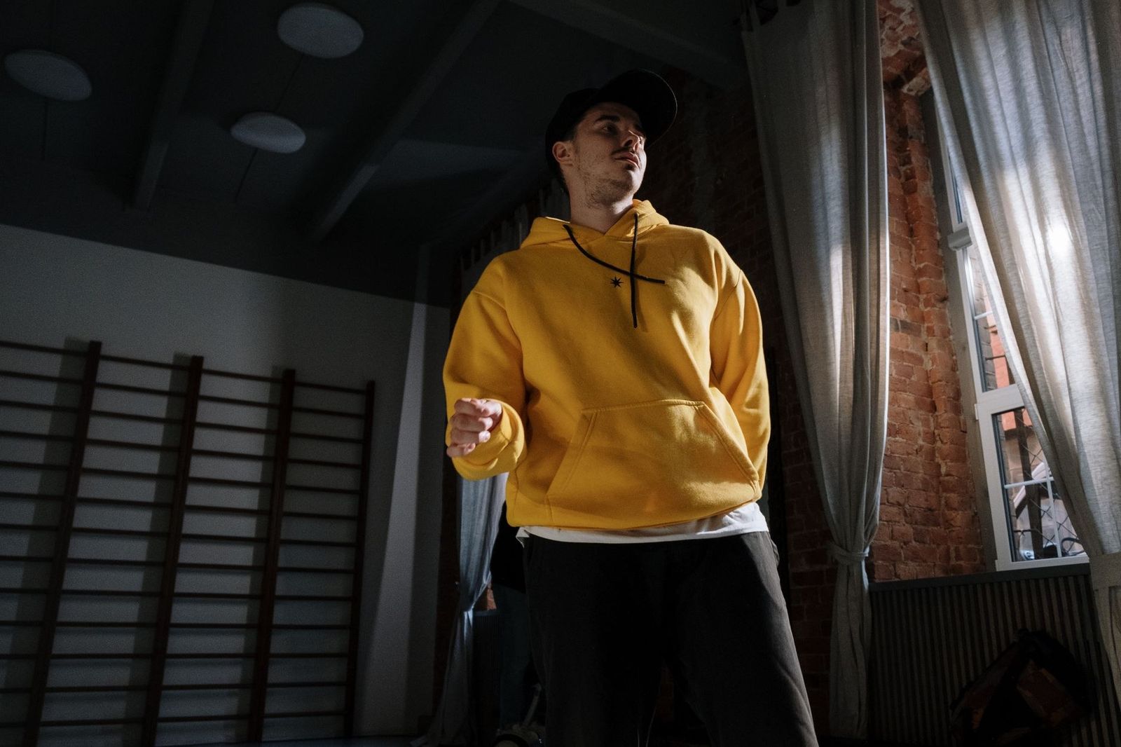 Man in yellow hoodie dancing indoors with dramatic lighting and shadows.