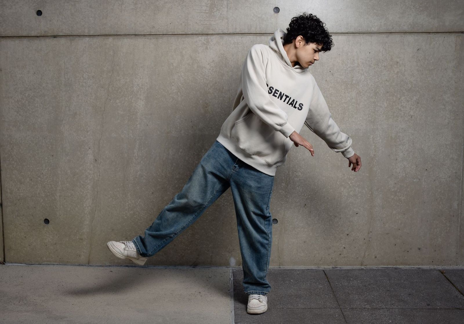 A teenager wearing a hoodie and jeans striking a fashionable pose indoors.