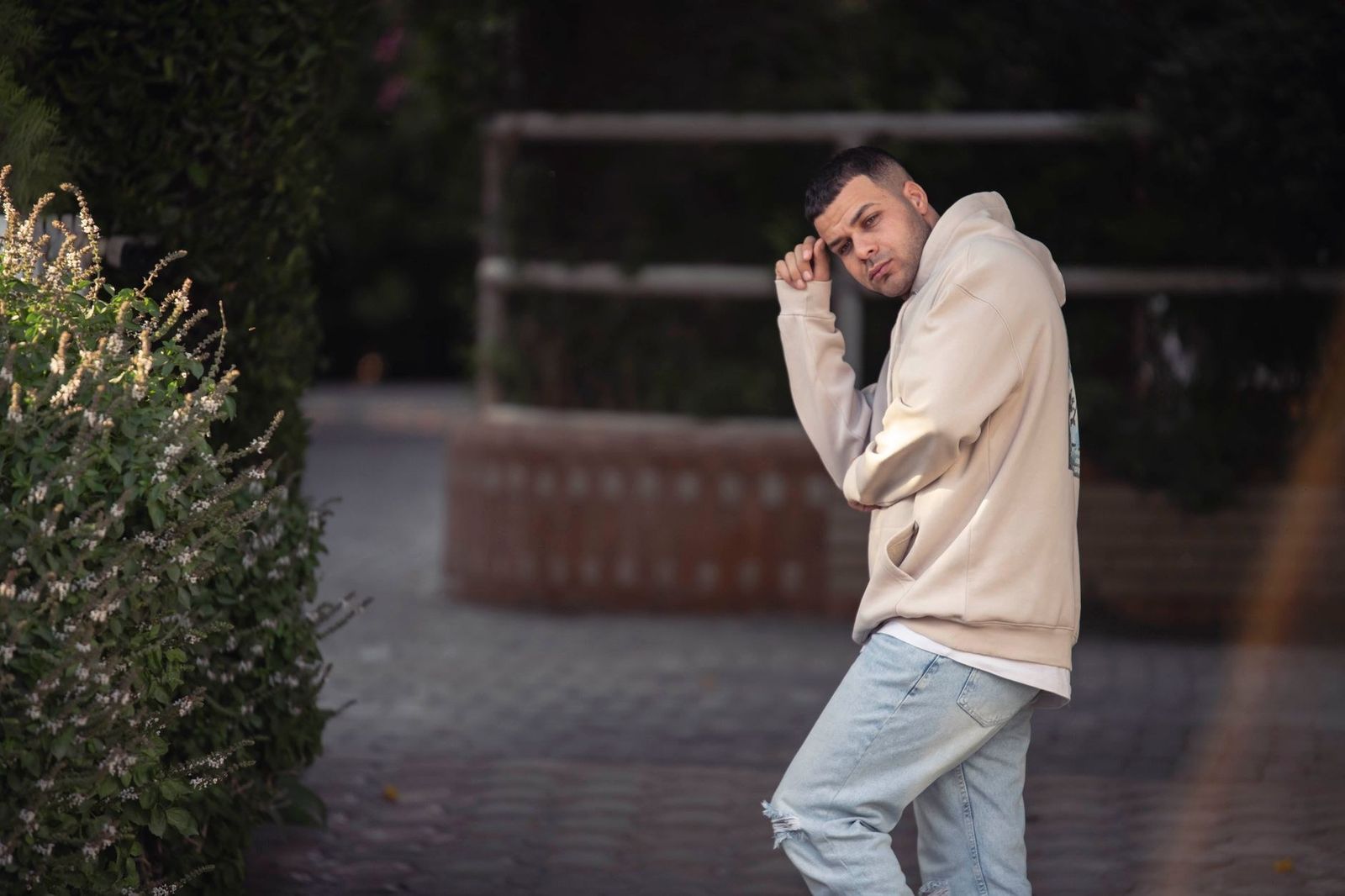 Young man posing in a hoodie and jeans in an outdoor setting reflecting urban style.