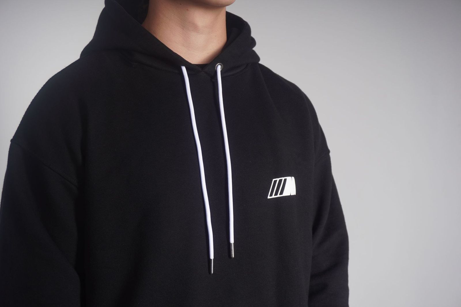 A minimalist shot of a person wearing a stylish black hoodie with a logo.