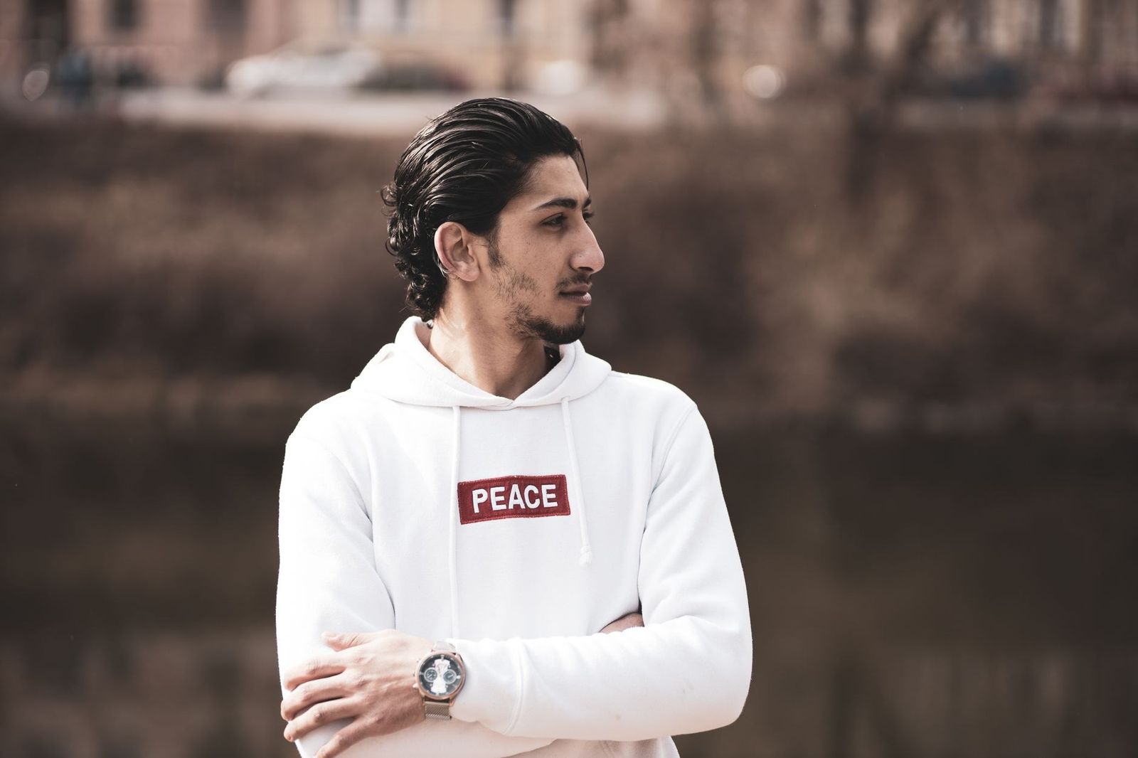 Young man with facial hair wearing a white hoodie posing outdoors.